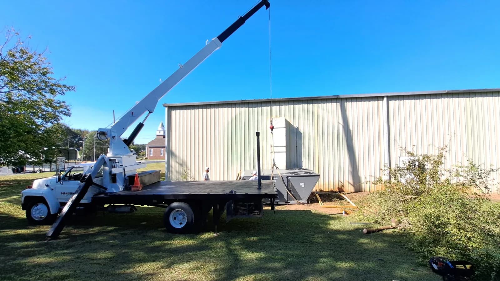 Boom truck lifting a large rooftop A/C unit at a metal building