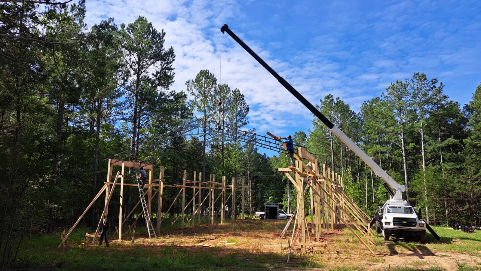 Boom truck with fully extended boom setting a steel truss on a post-frame building